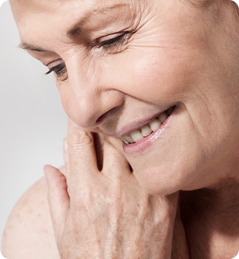 Woman smiling showing teeth, while her hand is feeling her face skin Woman smiling showing teeth, while her hand is feeling her face skin