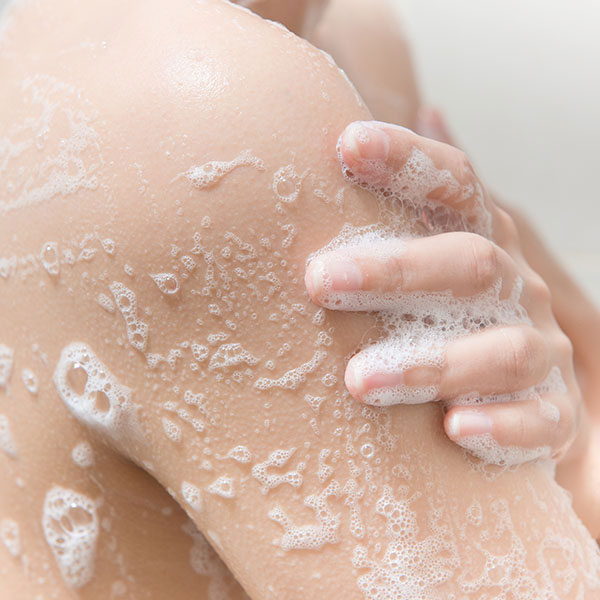 Woman rubbing her naked arm with soap and foam. 